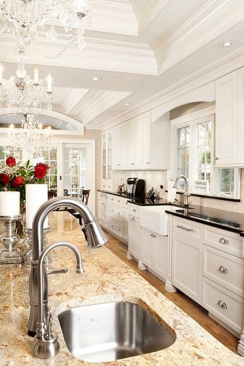 A kitchen with white cabinets , granite counter tops , a sink and a chandelier.