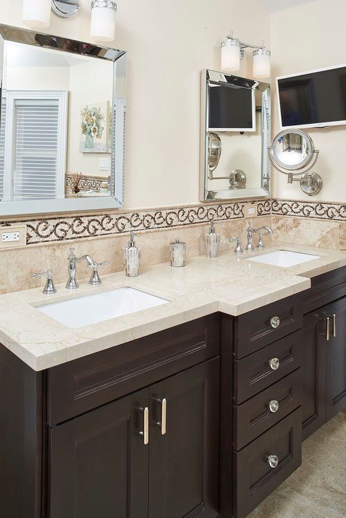 A bathroom with two sinks , two mirrors and a television.