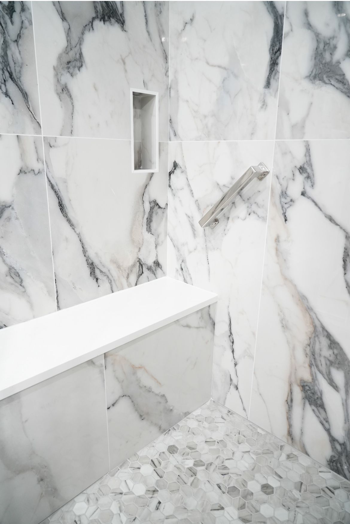 A shower with marble tiles and a bench in it.