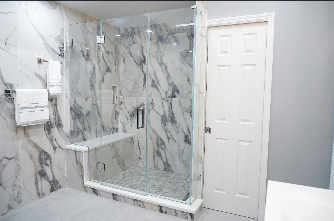 A bathroom with marble walls and a walk in shower with a glass door.