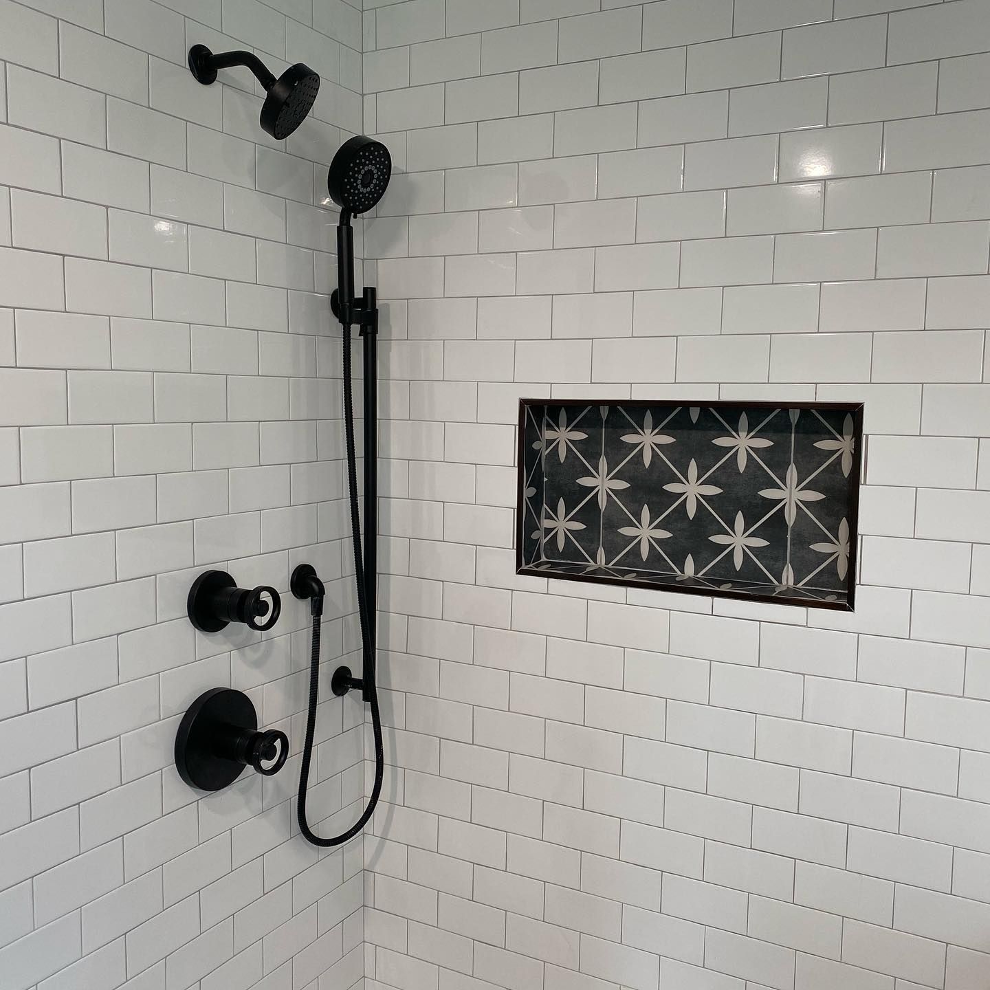 A shower with white tiles and a black shower head.
