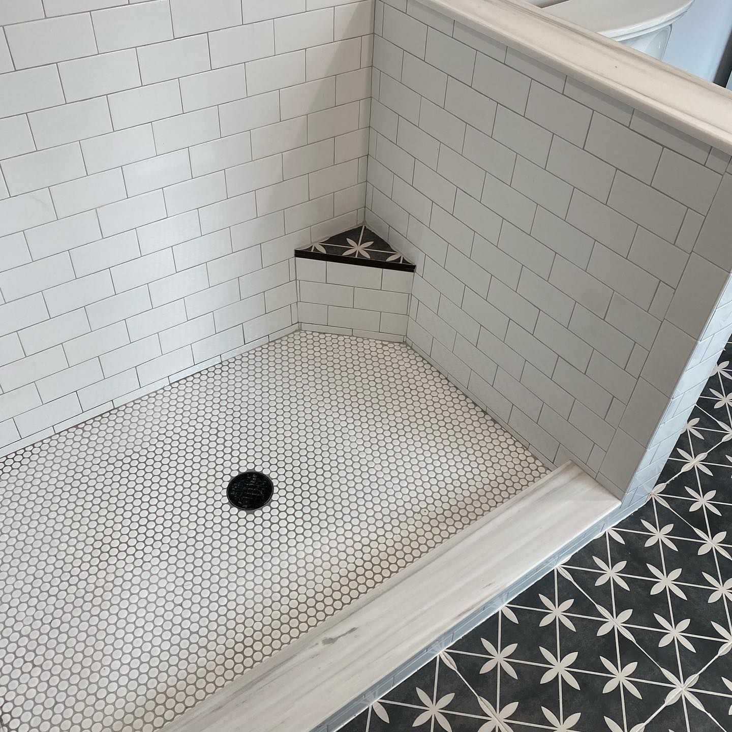 A shower stall with white tiles and a black drain