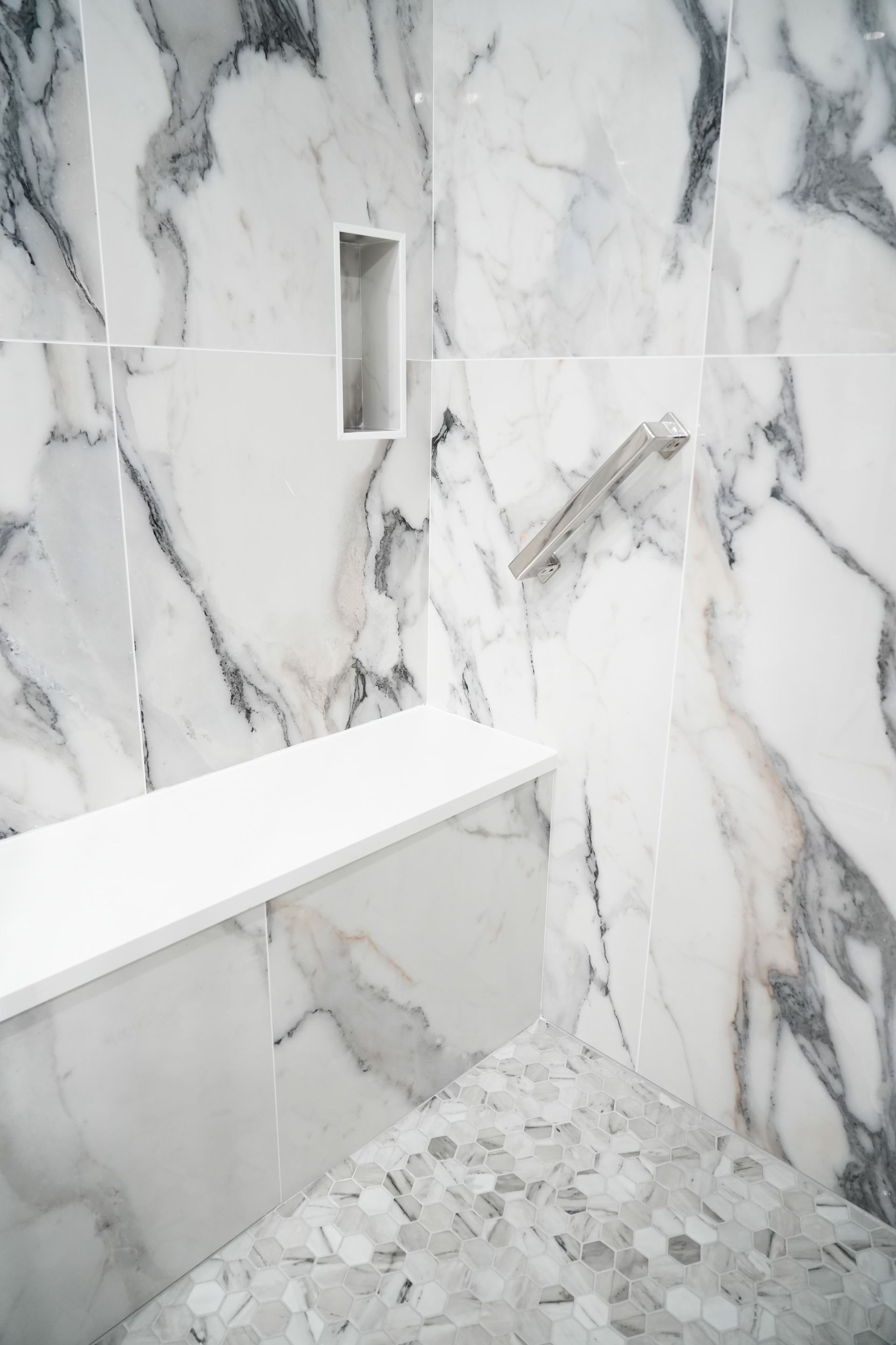 A bathroom with marble tiles and a shower with a bench.