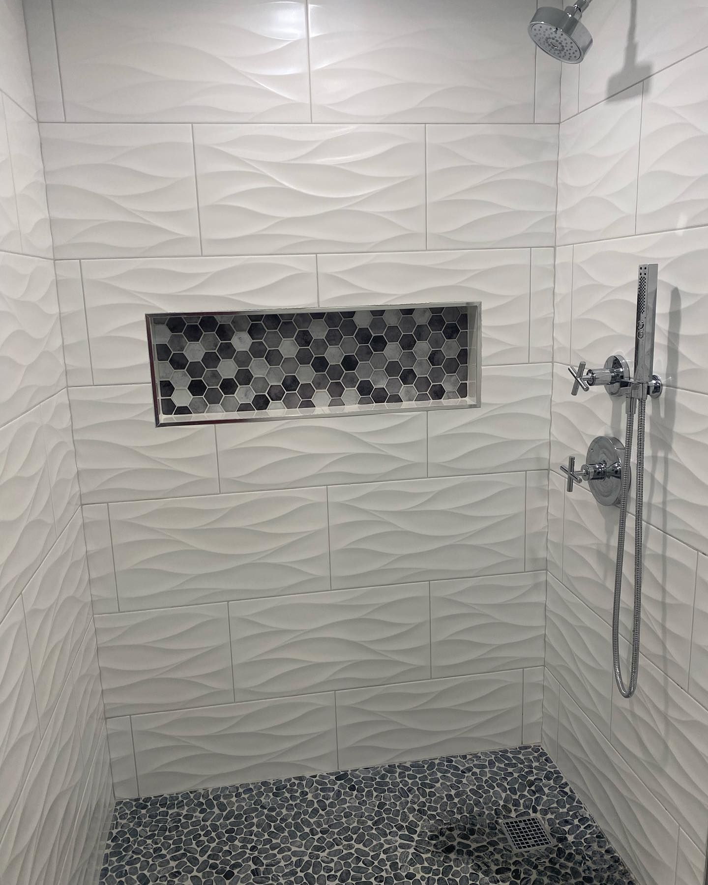 A shower with white tiles and a mosaic niche.