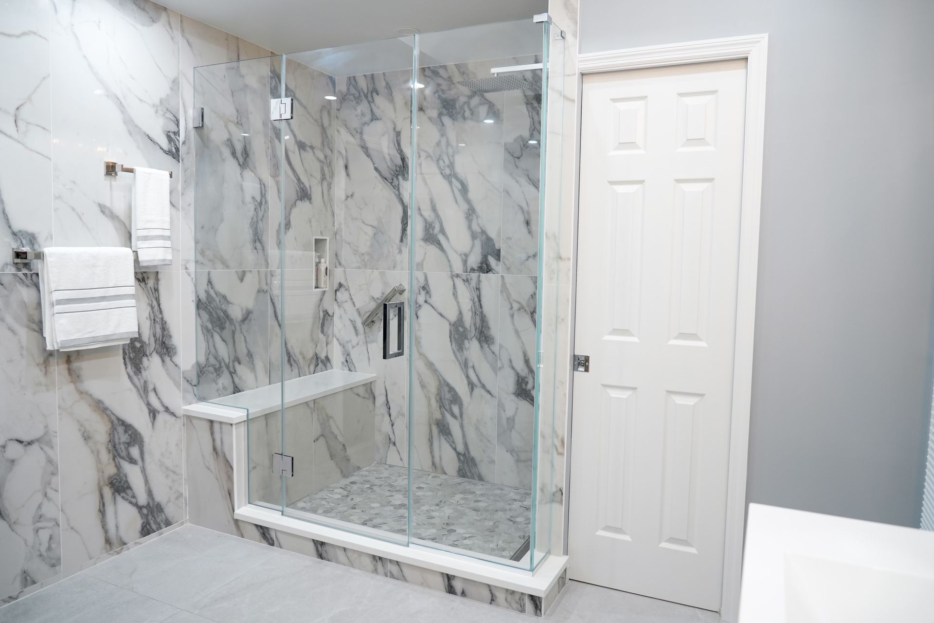 A bathroom with marble walls and a walk in shower with a glass door.