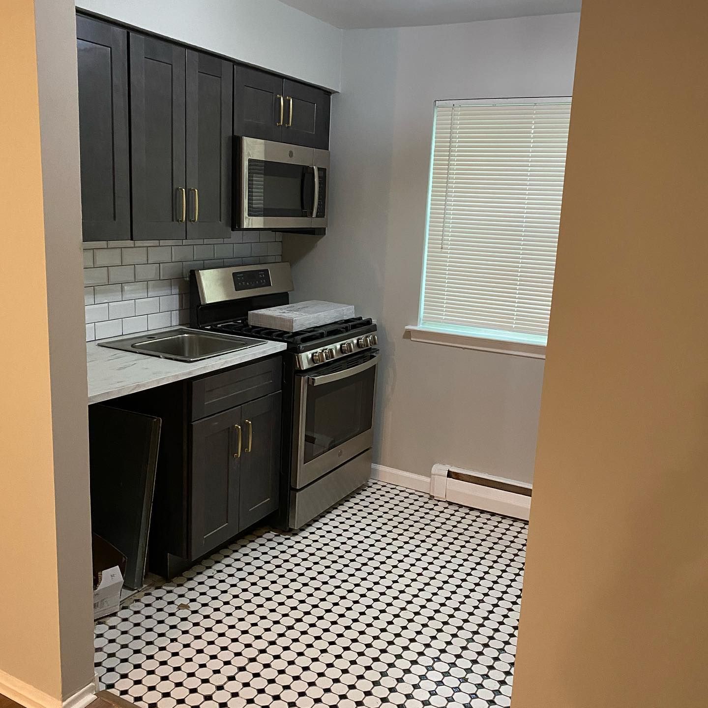 A kitchen with a stove , microwave , sink and window.