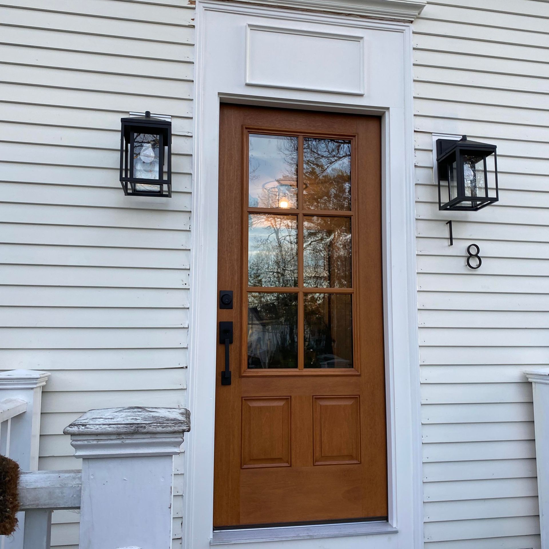 Wooden door with glass panels and sidelights; flanked by black lanterns. House number 18.