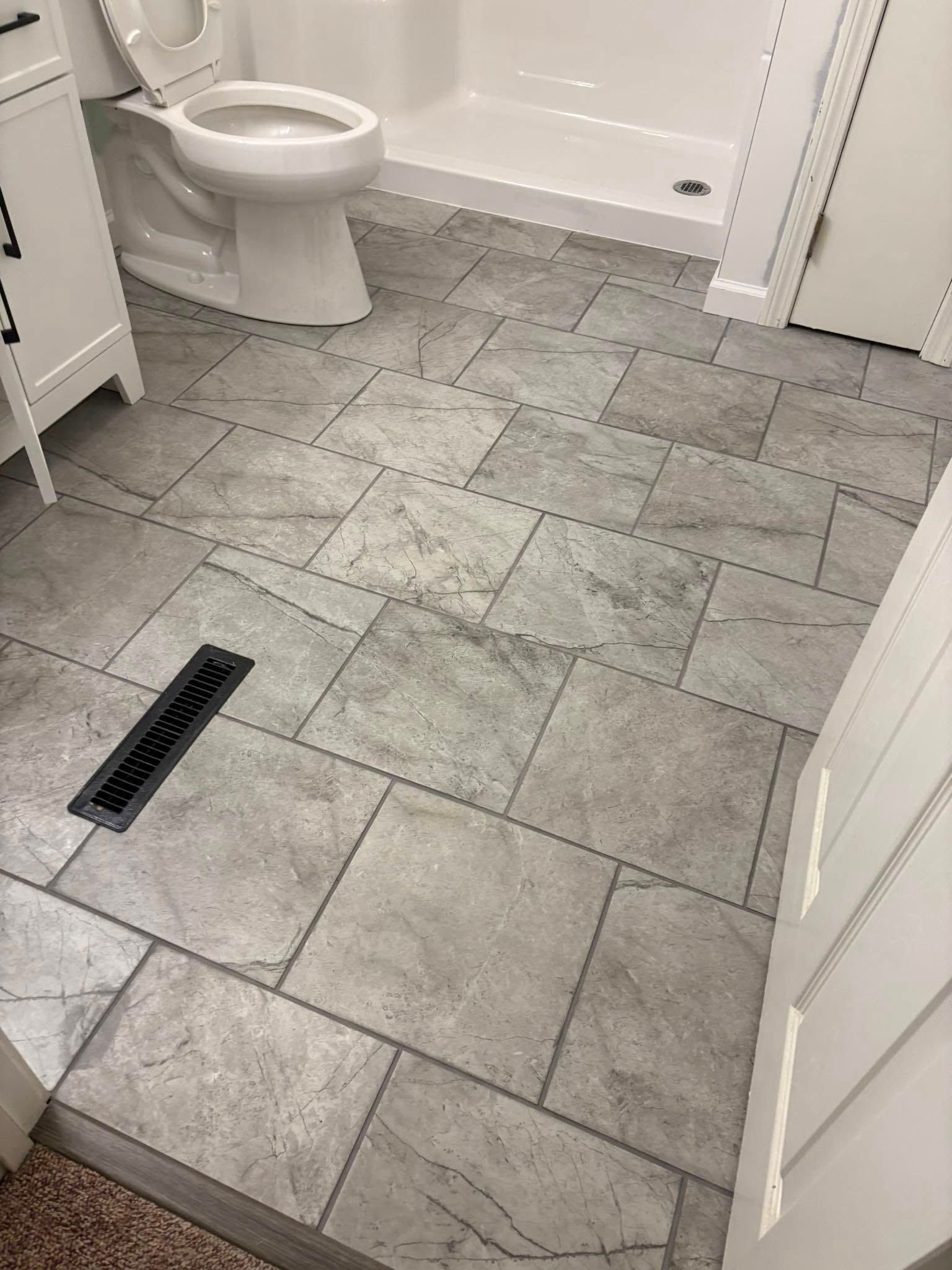 Bathroom with gray tiled floor, white toilet and shower, and white cabinets.