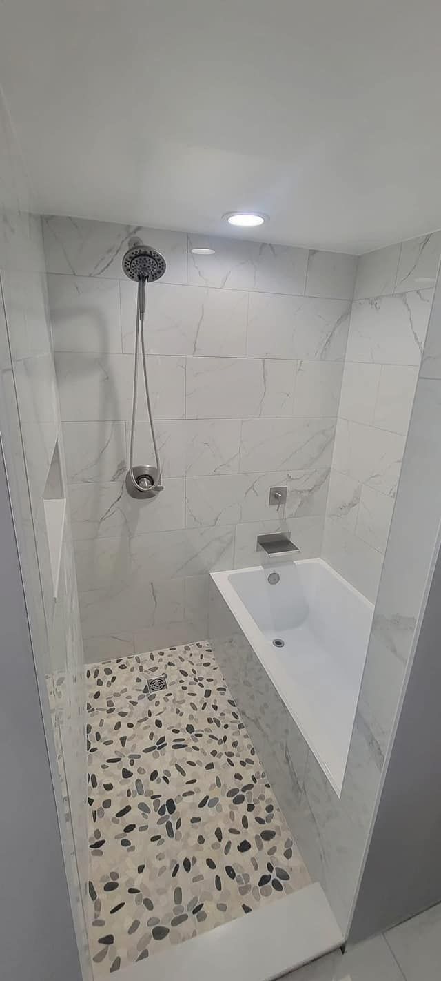Modern bathroom with pebble-stone shower floor, marble-tiled walls, and built-in bathtub.