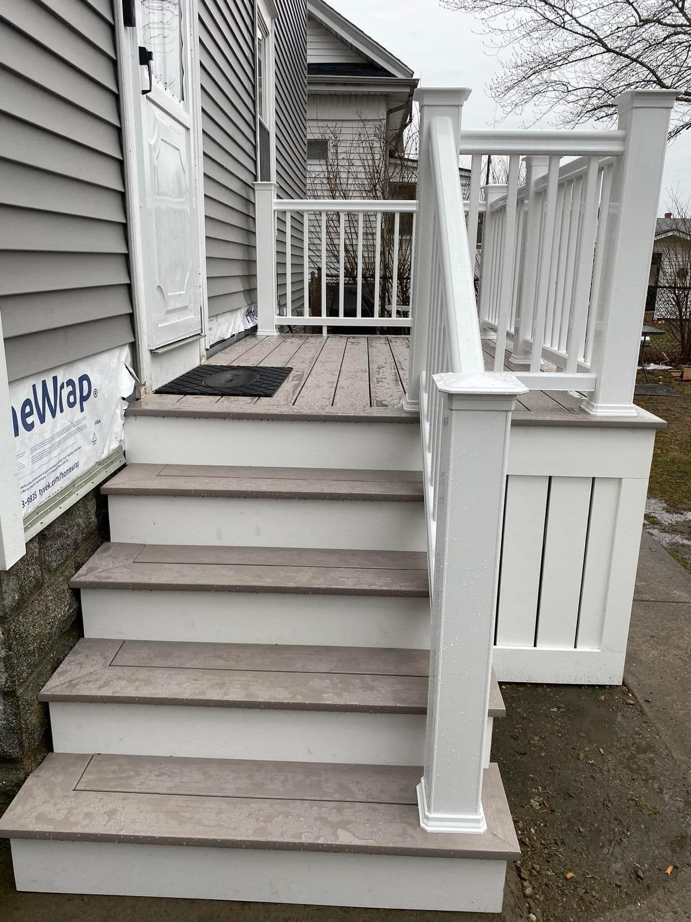 Gray wooden steps lead to a white railed deck in front of a gray house.