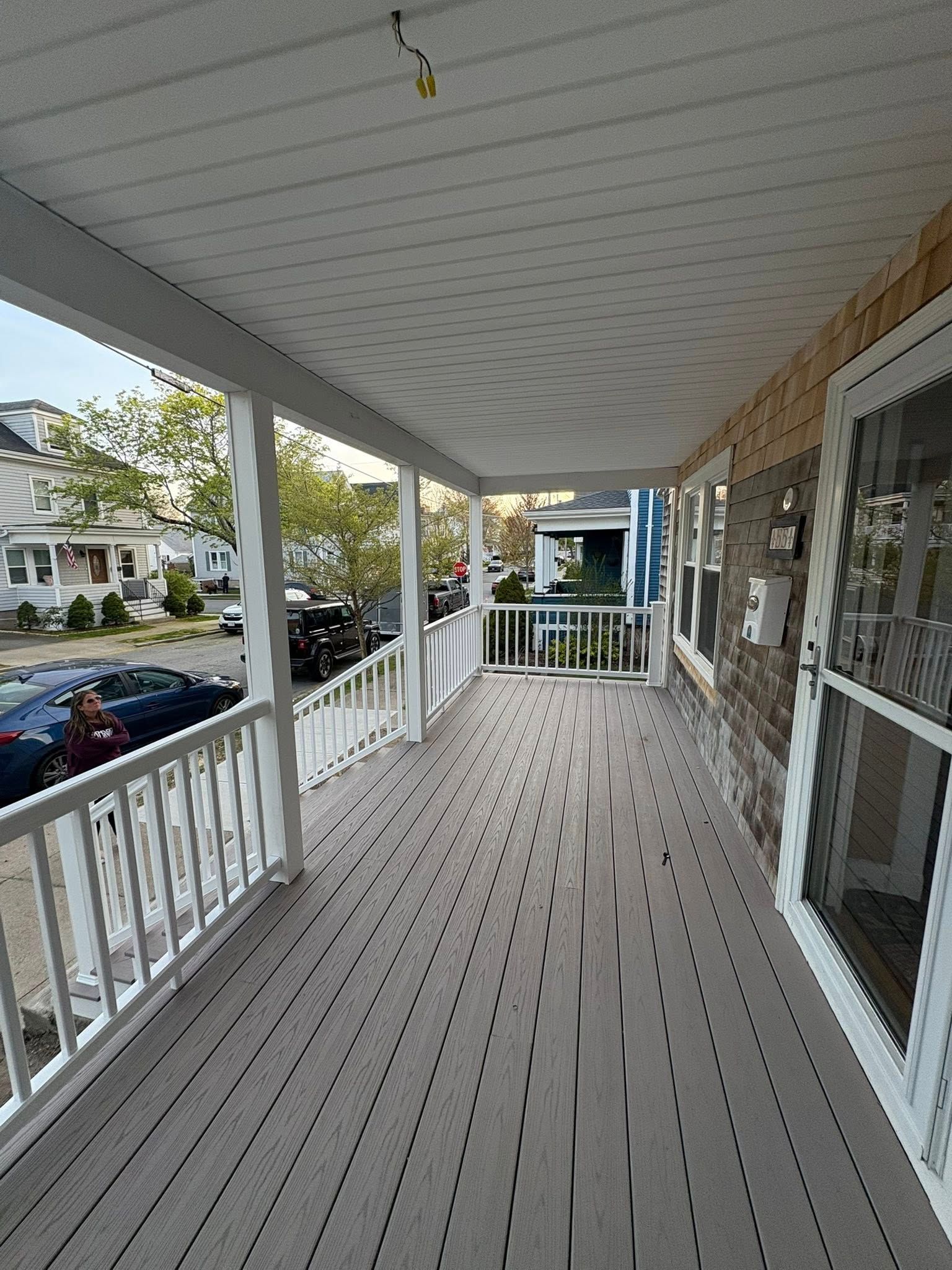 Covered porch with gray decking, white railings, and street view.