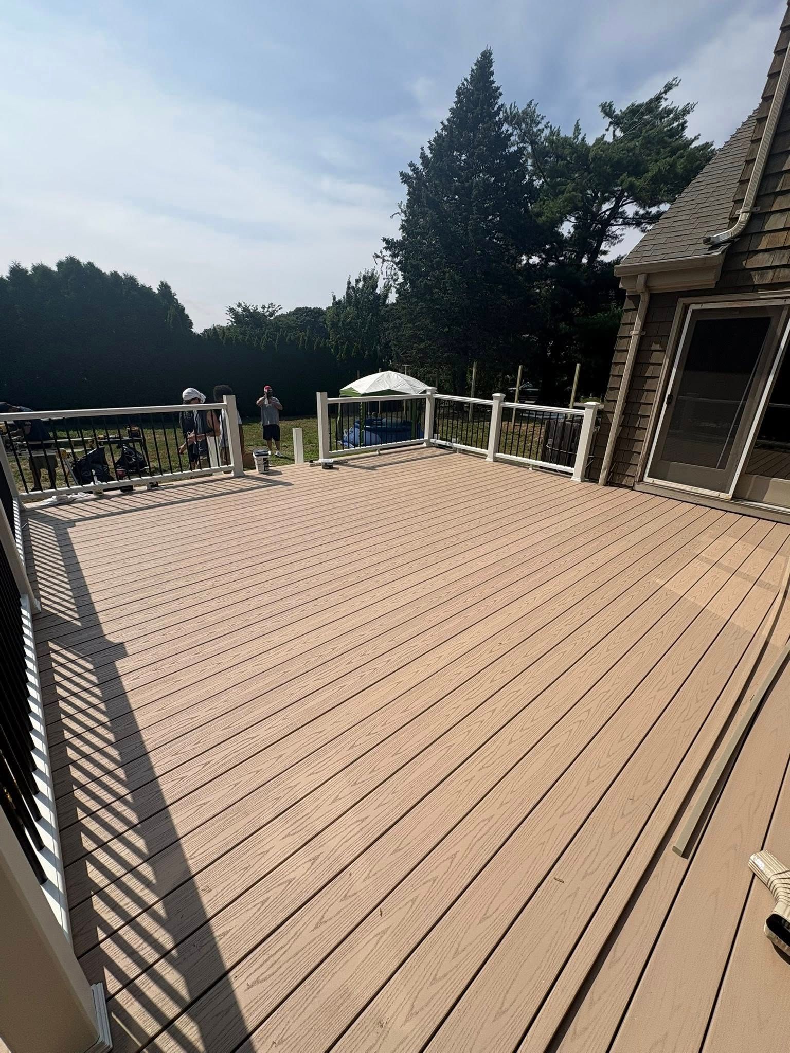 Wooden deck with white railing, gazebo in background, sunny day.