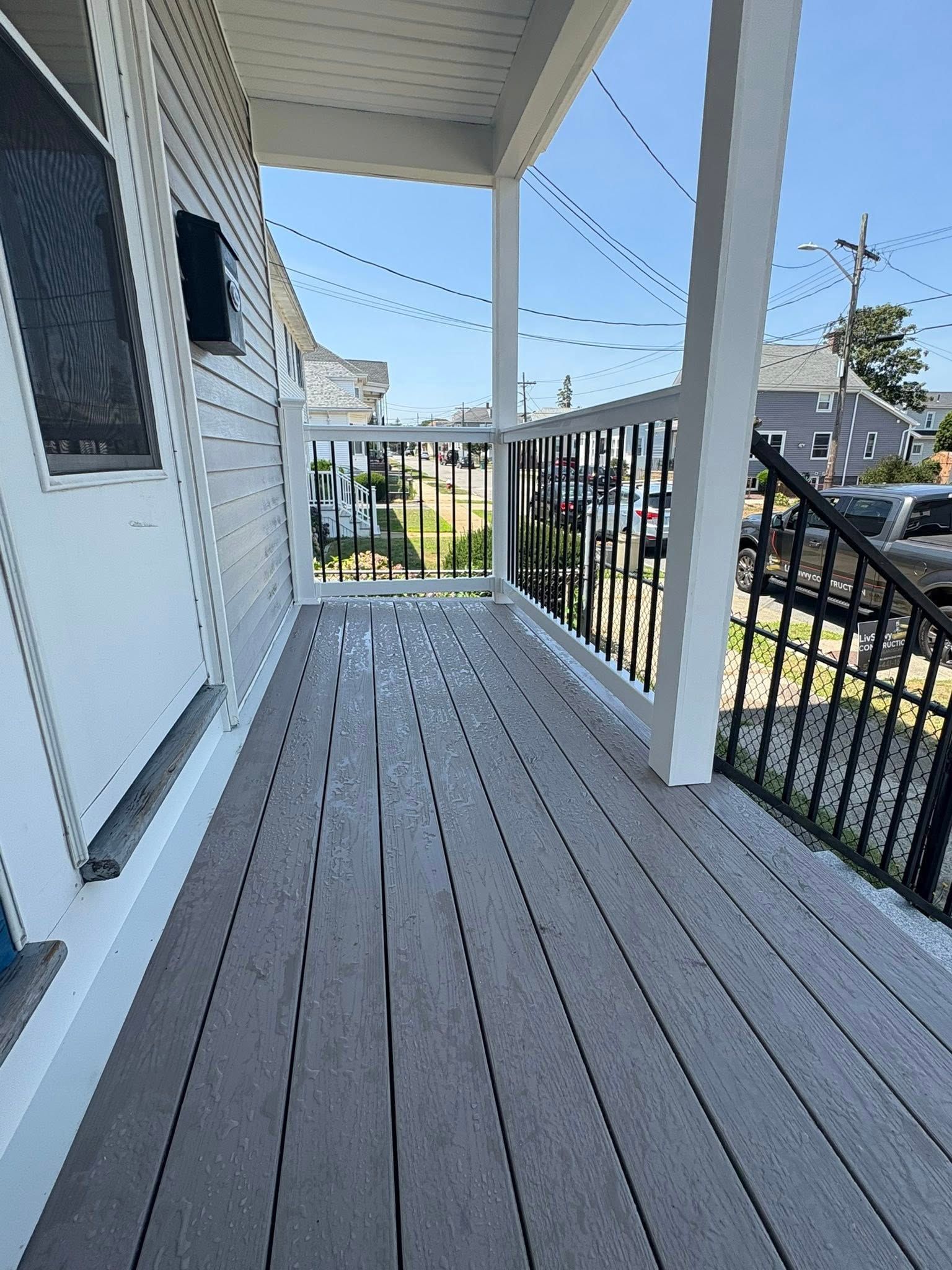Gray composite porch with black railings, white posts, and clear sky.