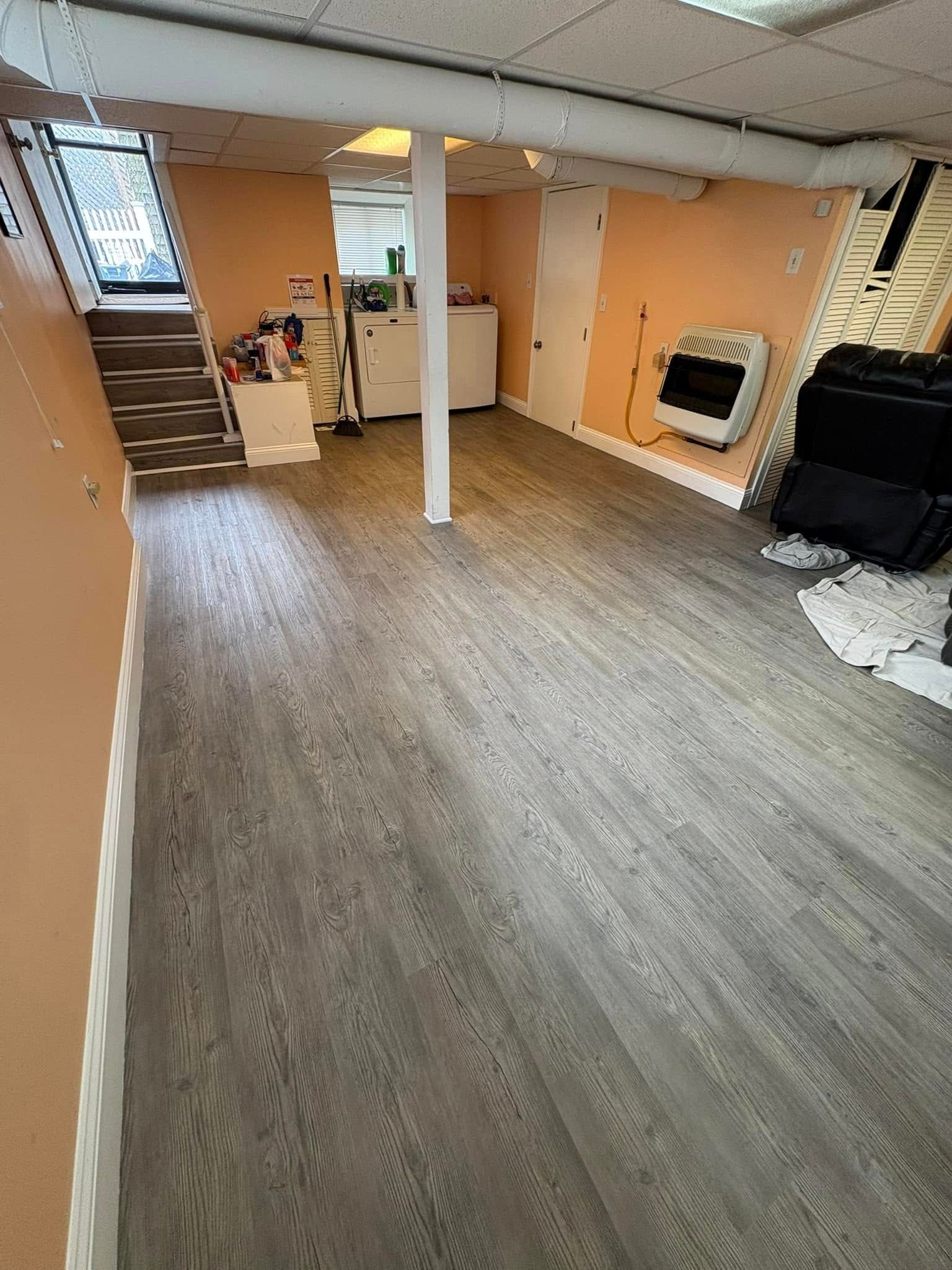 Basement with wood-look flooring, off-white walls, stairs, a heater, and a support column.