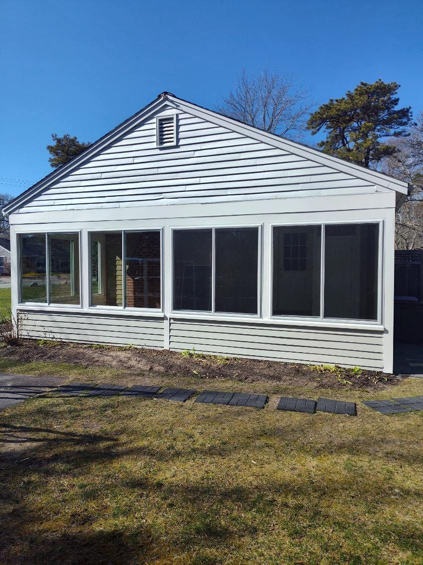 White screened porch with multiple windows; grassy yard, blue sky.