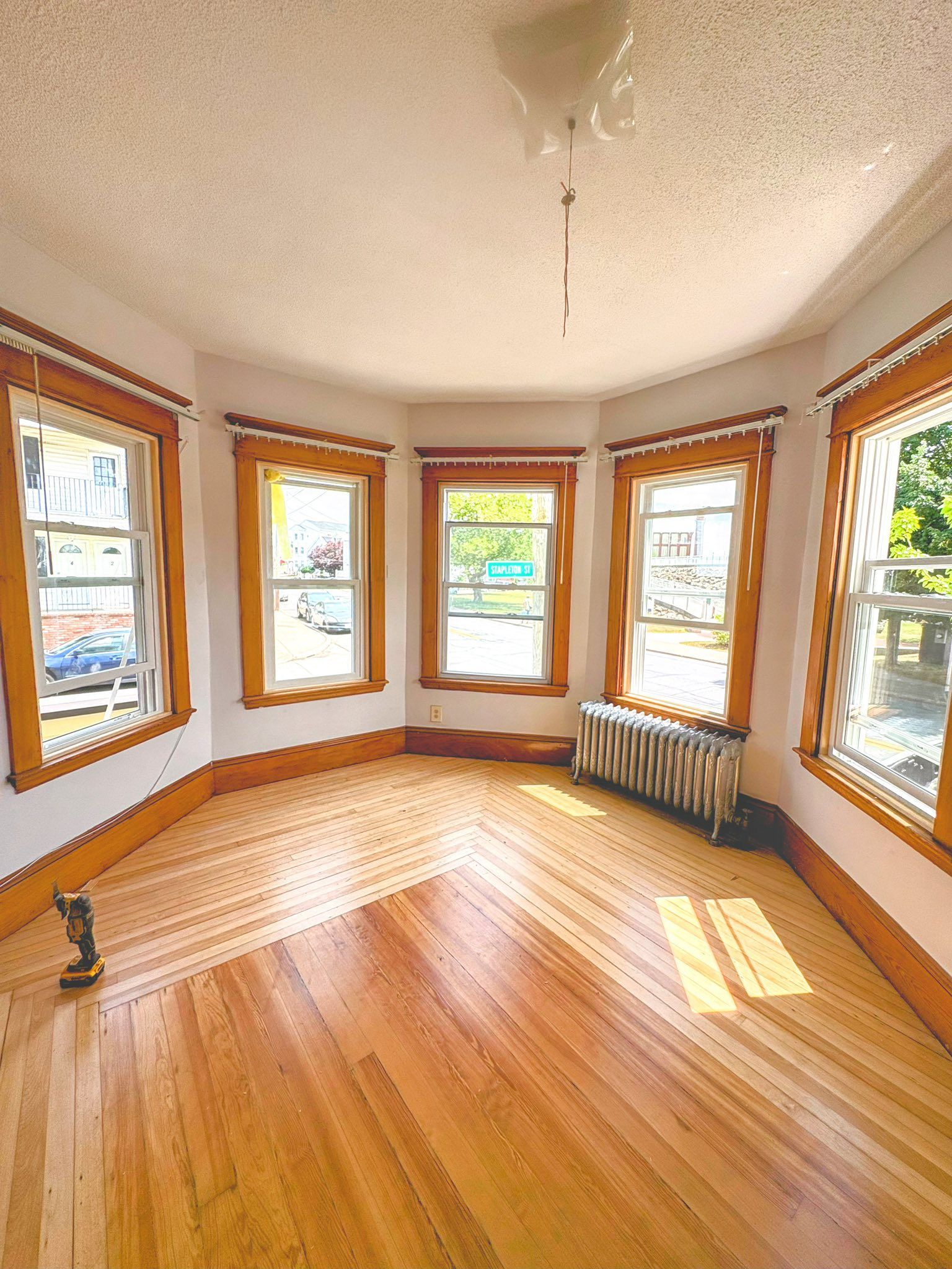 Empty room with hardwood floors, windows, radiator, and a ceiling light.