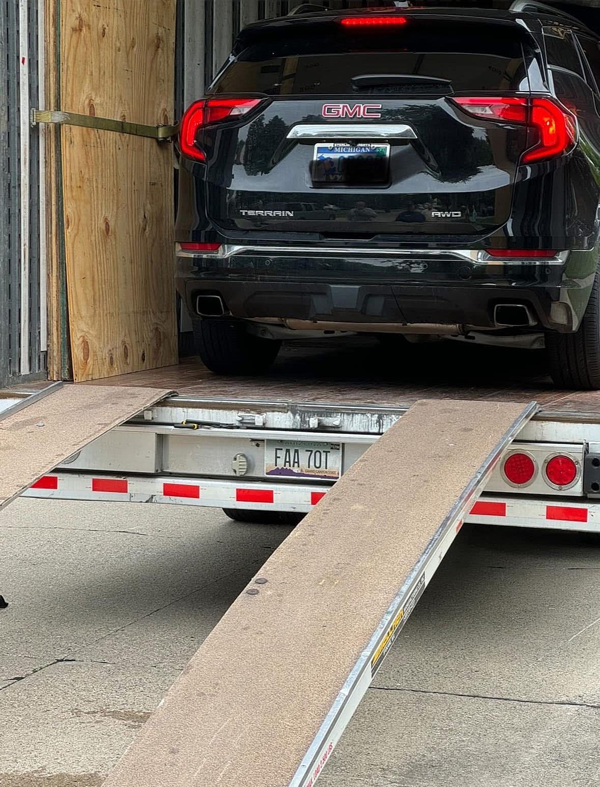 Black GMC SUV on a car hauler trailer, backed into a cargo container.