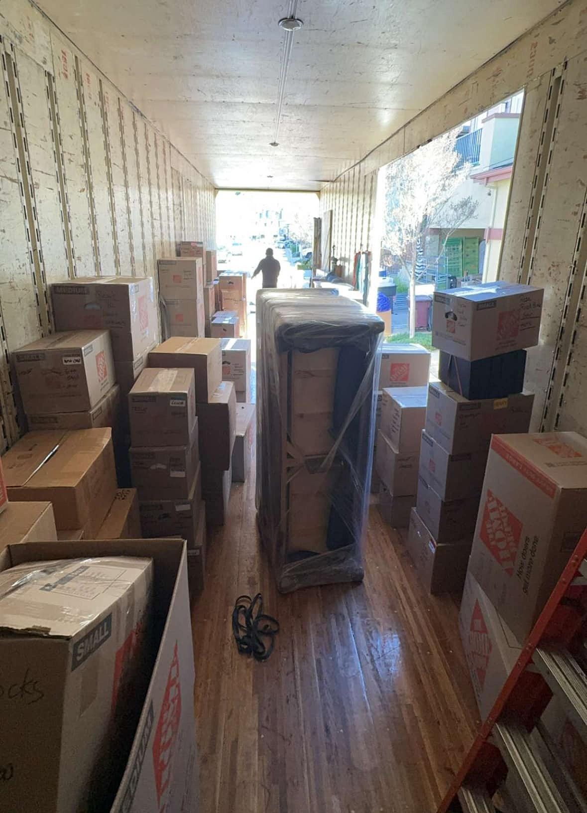 Boxes and wrapped furniture fill a moving truck, with a person standing near the open door.