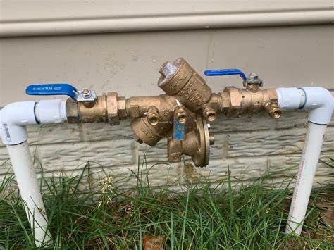 A water valve is attached to a pipe outside of a house.