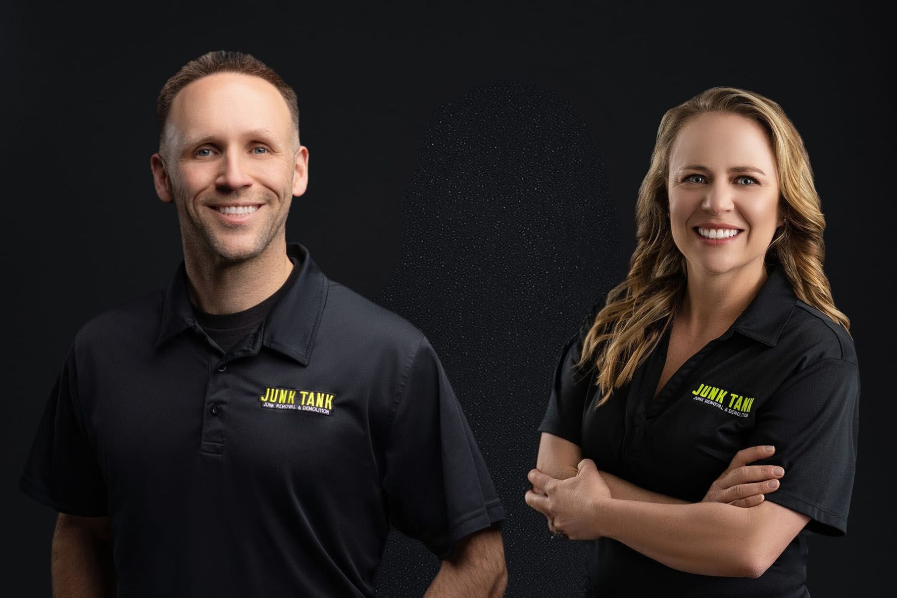 Two smiling professionals in black polo shirts with yellow branding stand side-by-side against a black background.