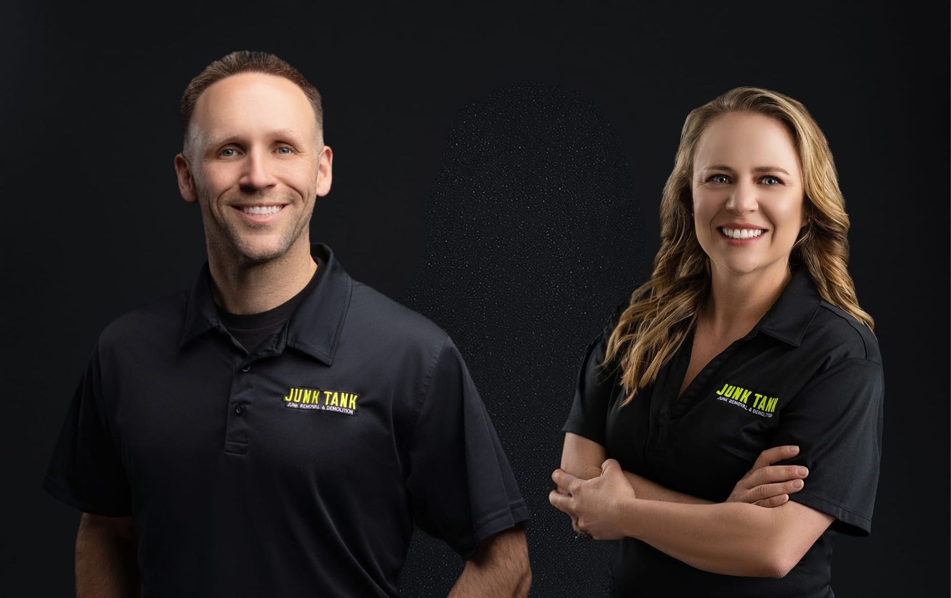 Two smiling professionals in black polo shirts with yellow branding stand side-by-side against a black background.