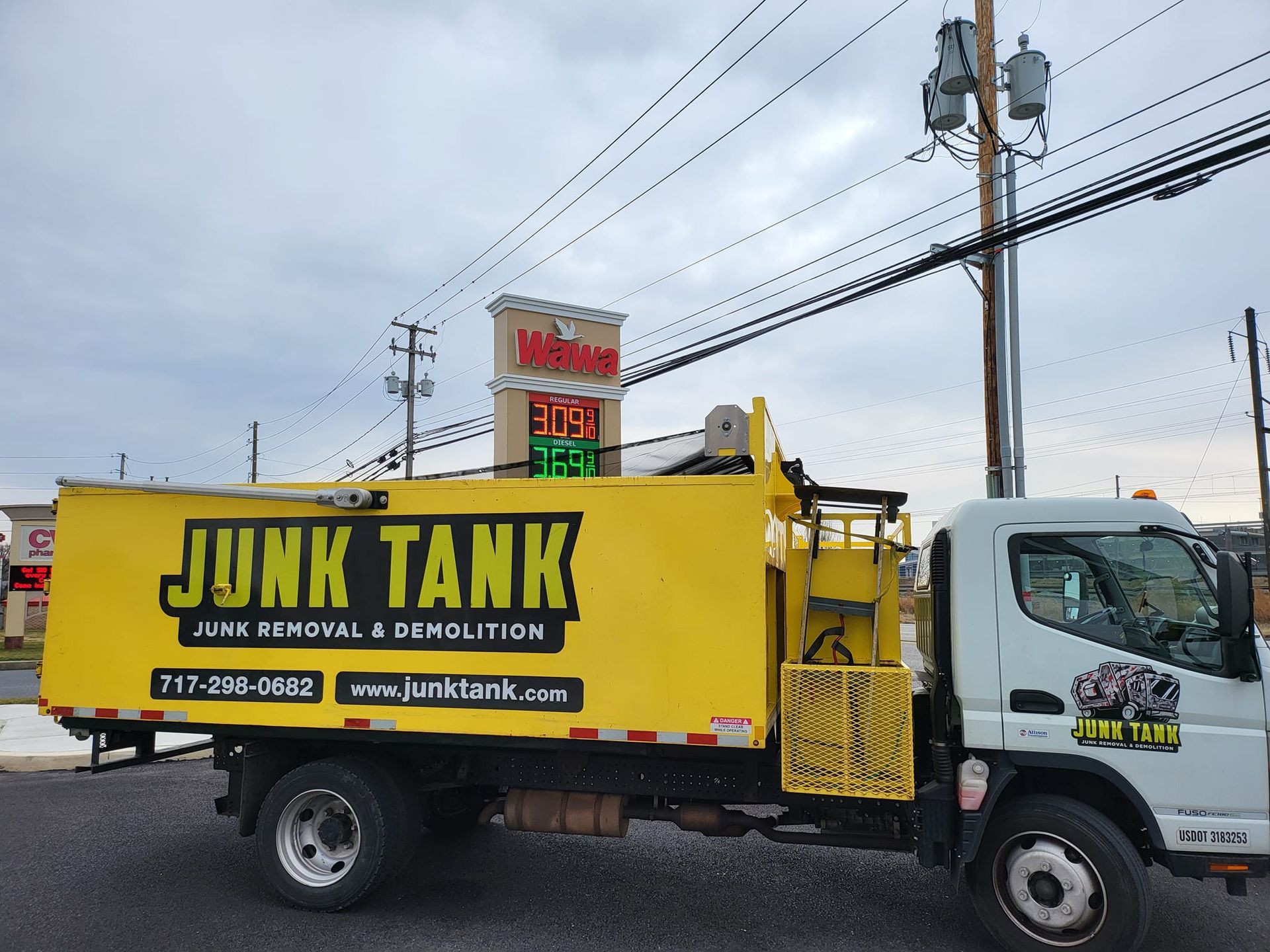 Yellow "JUNK TANK" truck for junk removal and demolition parked on a street near a building with a red sign.