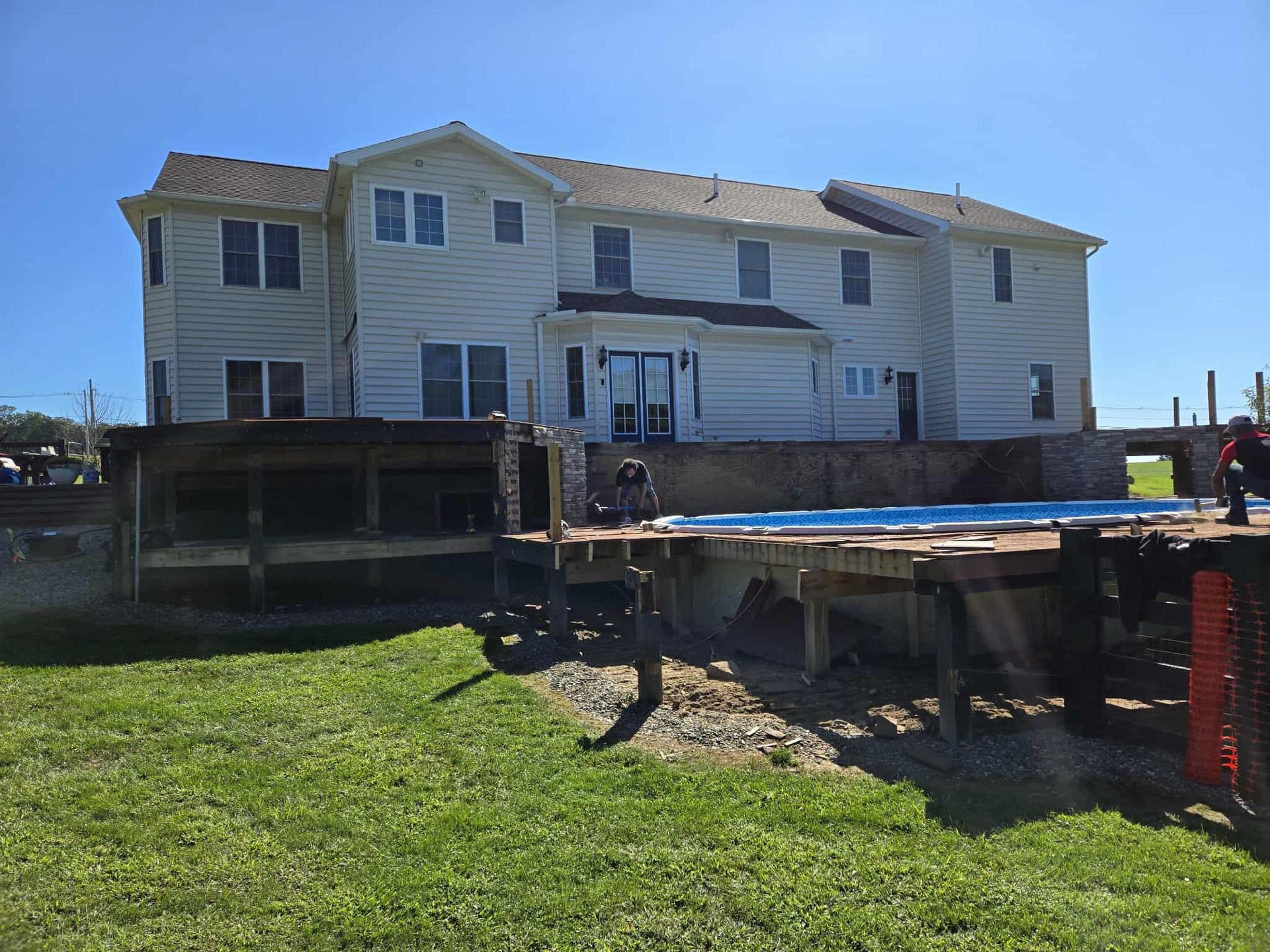 Back of a large, two-story house with a wooden deck and in-ground pool; sunny day.