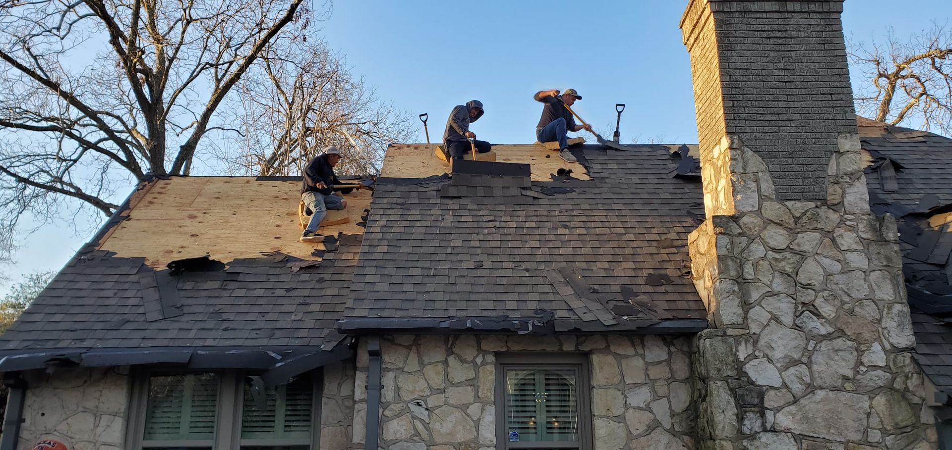 A group of men are working on the roof of a stone house.