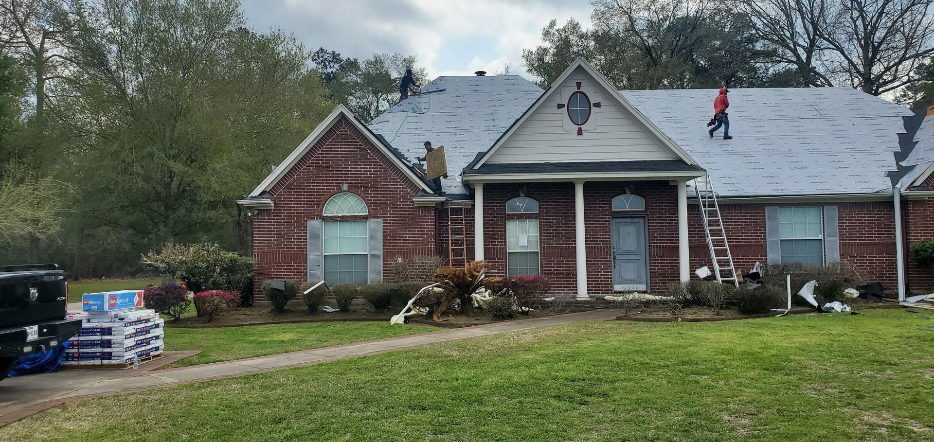 Two men are working on the roof of a brick house.