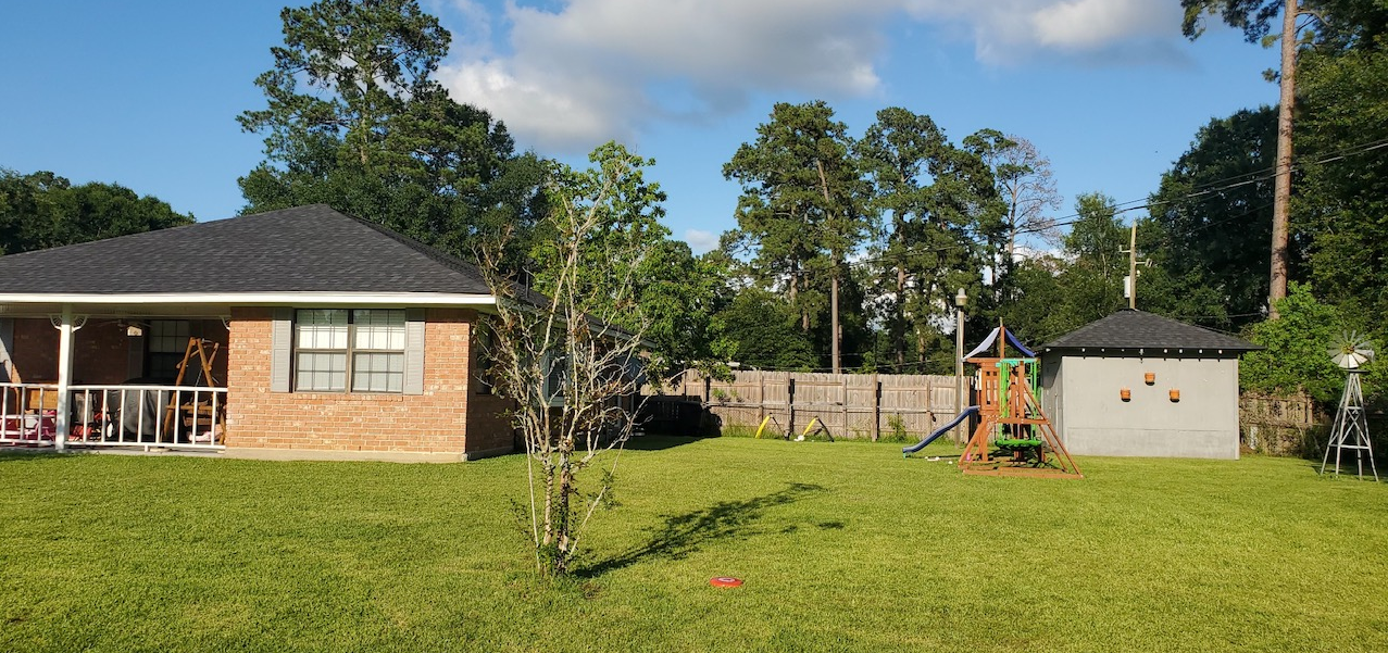 A brick house with a large lawn in front of it and a playground in the backyard.