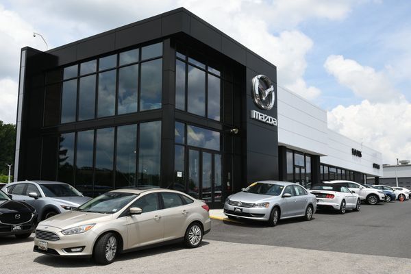 Mazda car dealership exterior with parked cars. Black building with large windows, Mazda logo.