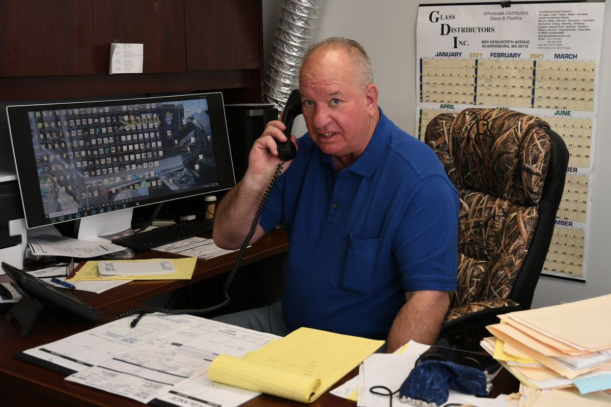 Man on phone at desk, looking concerned. Office setting, computer monitor showing screen, cluttered desk.