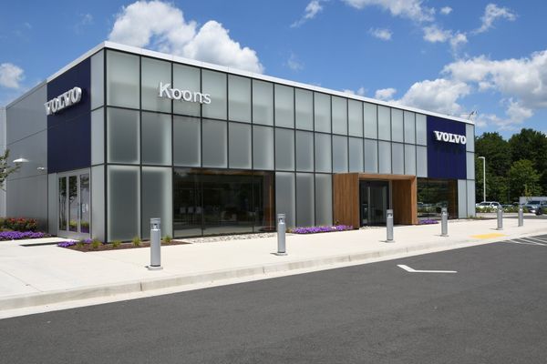 Volvo dealership with glass facade, Koons sign, blue and white accents, sunny day.