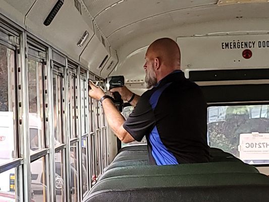 Person inspecting a school bus window with a tool. Interior shot.