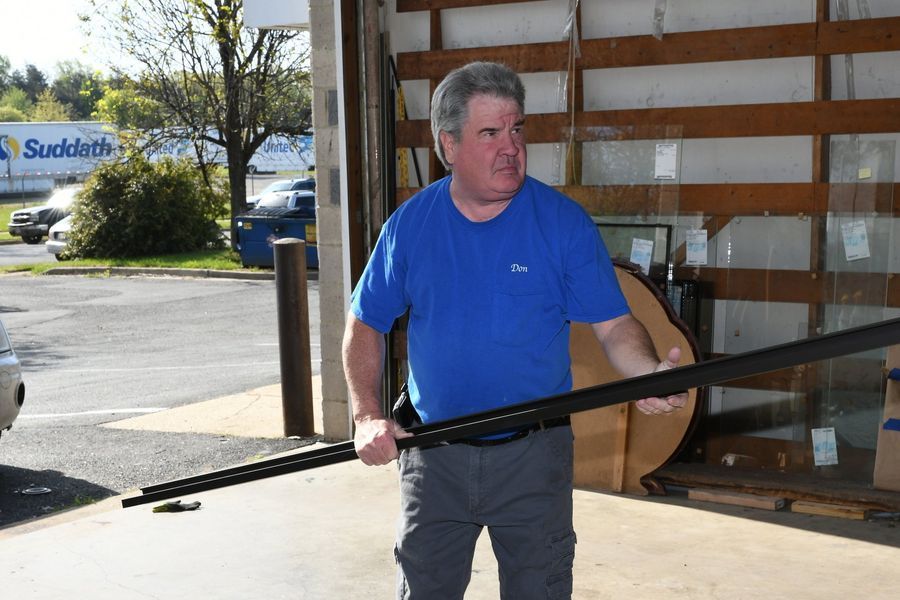 Man in blue shirt holding long, dark metal bars in a warehouse setting.
