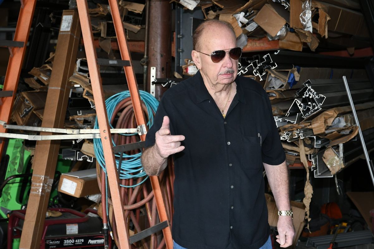 Man in sunglasses and black shirt points, standing in a cluttered garage.