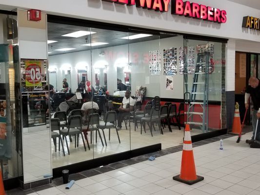 Barbershop interior, glass storefront. People inside, chairs set out. Orange traffic cones and ladder visible. 