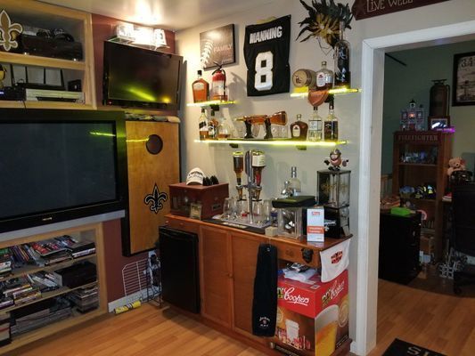 Home bar with liquor bottles, sports memorabilia, a TV, and a mini-fridge.