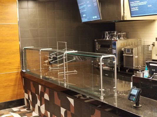 A cafe counter with a glass barrier and payment terminal. Dark tiles on the wall, menu boards above.