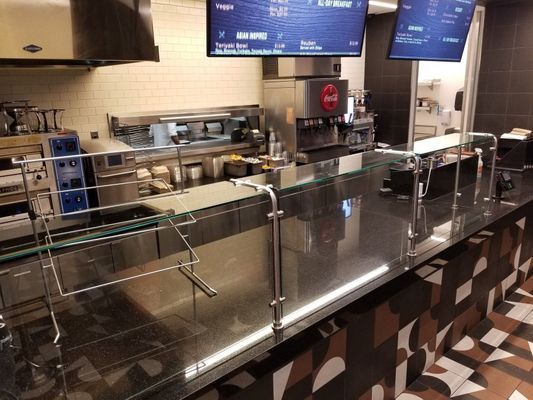 Empty restaurant food counter with menu boards, soda machine, and glass sneeze guards.