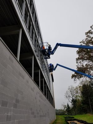 Two blue boom lifts next to a building installing metal or glass on the upper facade.