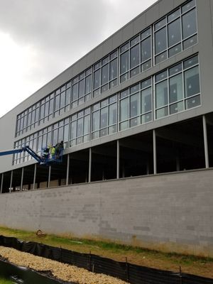Exterior of a two-story building under construction; workers in a lift, installing windows. Gray building with concrete foundation.