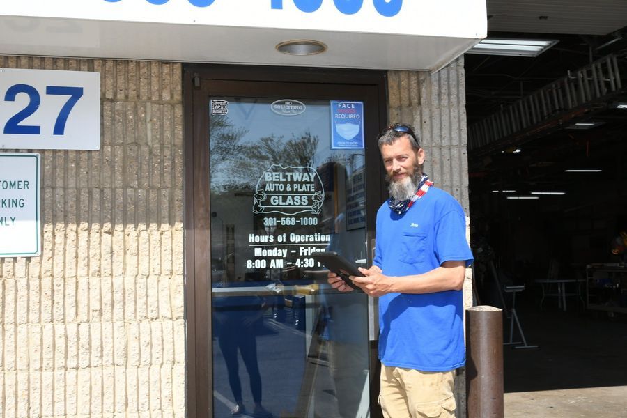 Man in blue shirt holding tablet, standing outside a business, 