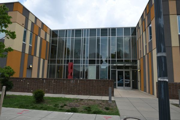 Modern building with large glass entrance, flanked by colorful patterned walls, brick base, and sidewalk.