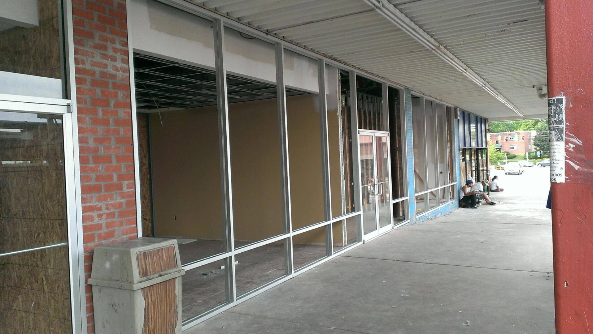 Exterior of a building under renovation with exposed metal framing and broken windows. Red brick and a concrete walkway are visible.