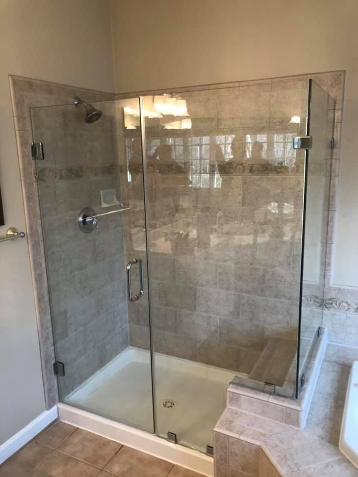 Glass shower enclosure with gray tile walls and white base. Chrome fixtures and handle.