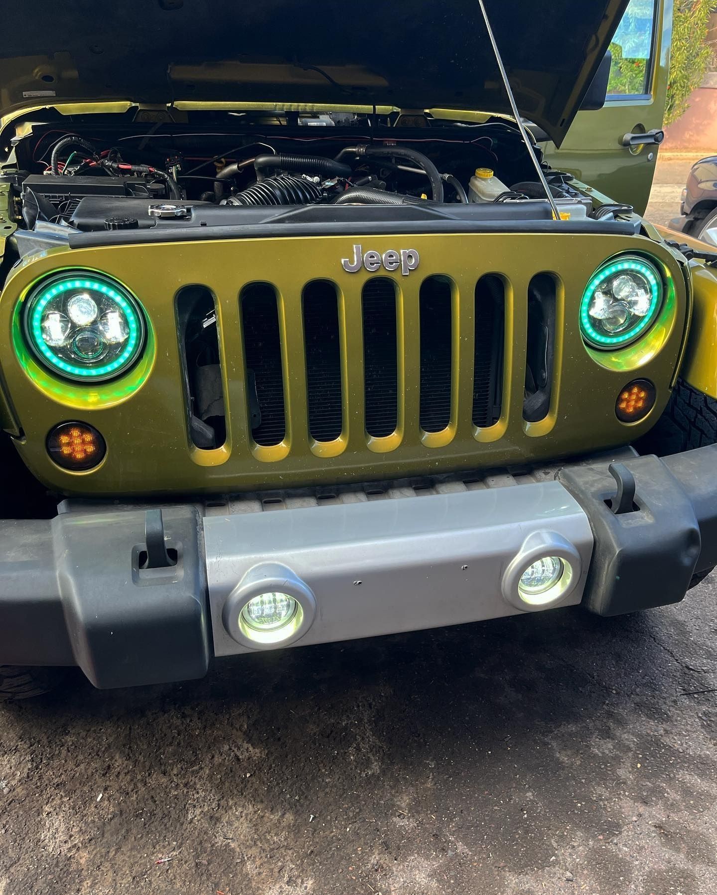 A green jeep with the hood open is parked on the side of the road.