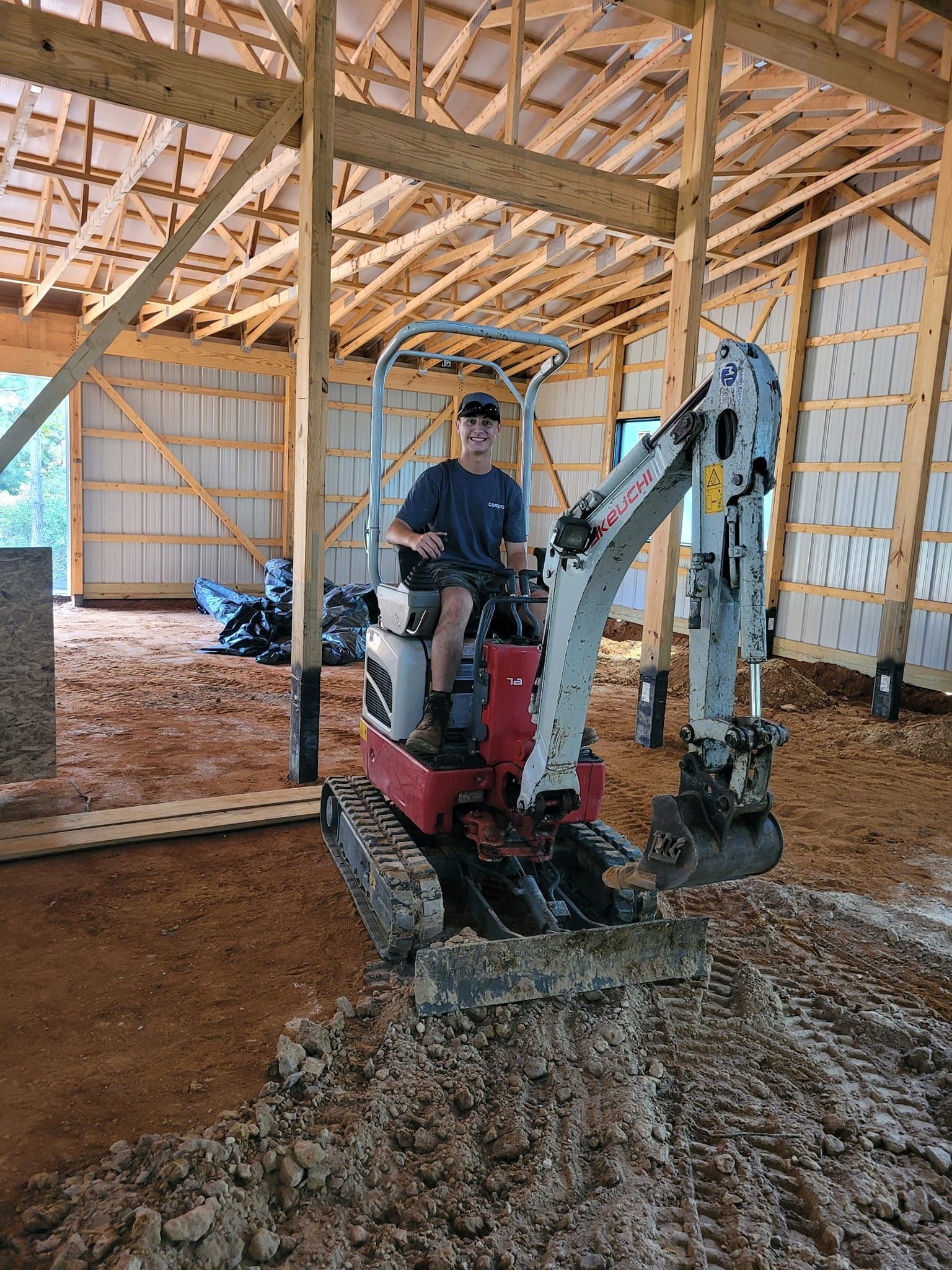 A man is sitting on a small excavator in a building under construction.
