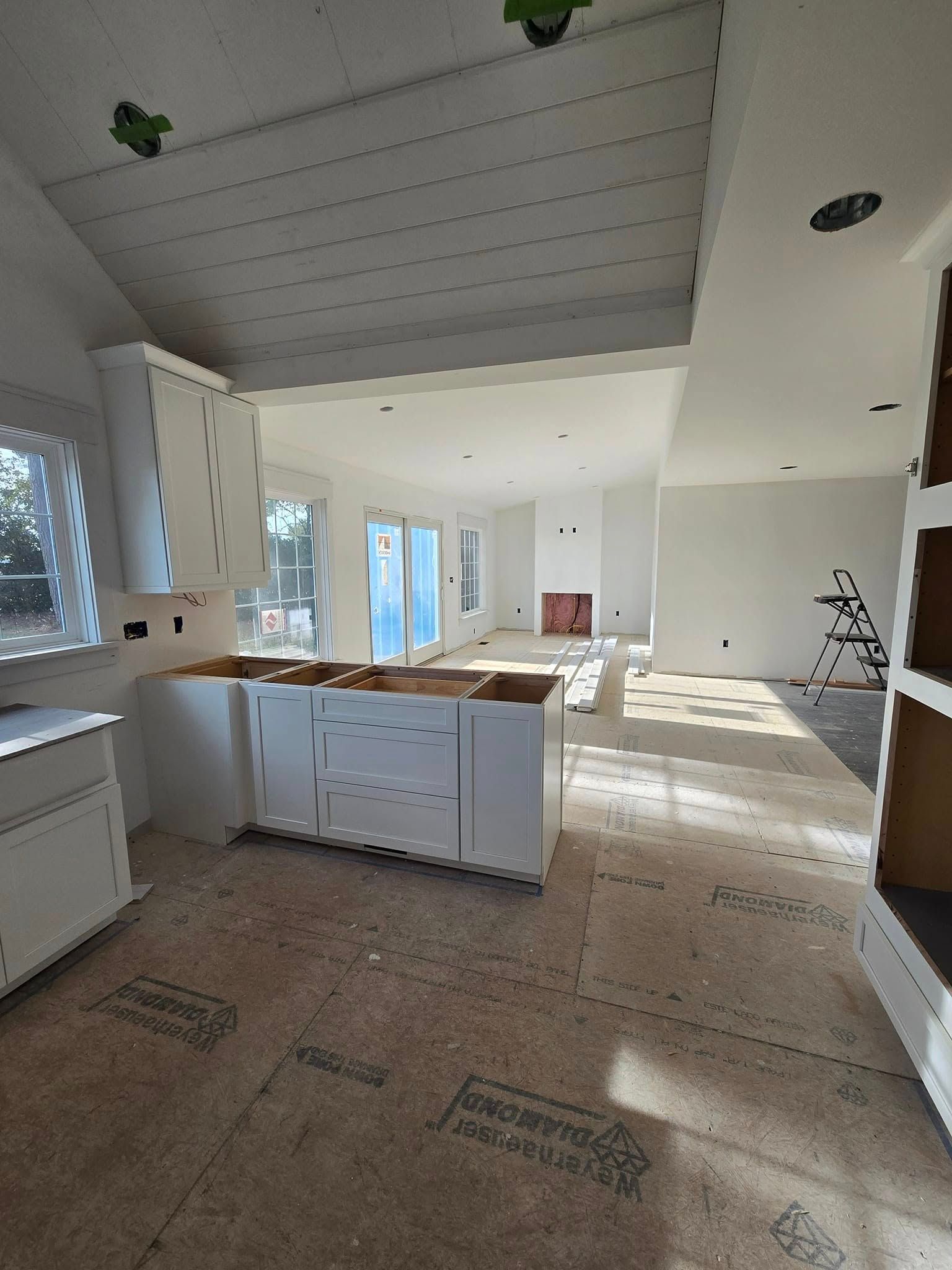 A kitchen under construction with white cabinets and a wooden floor.
