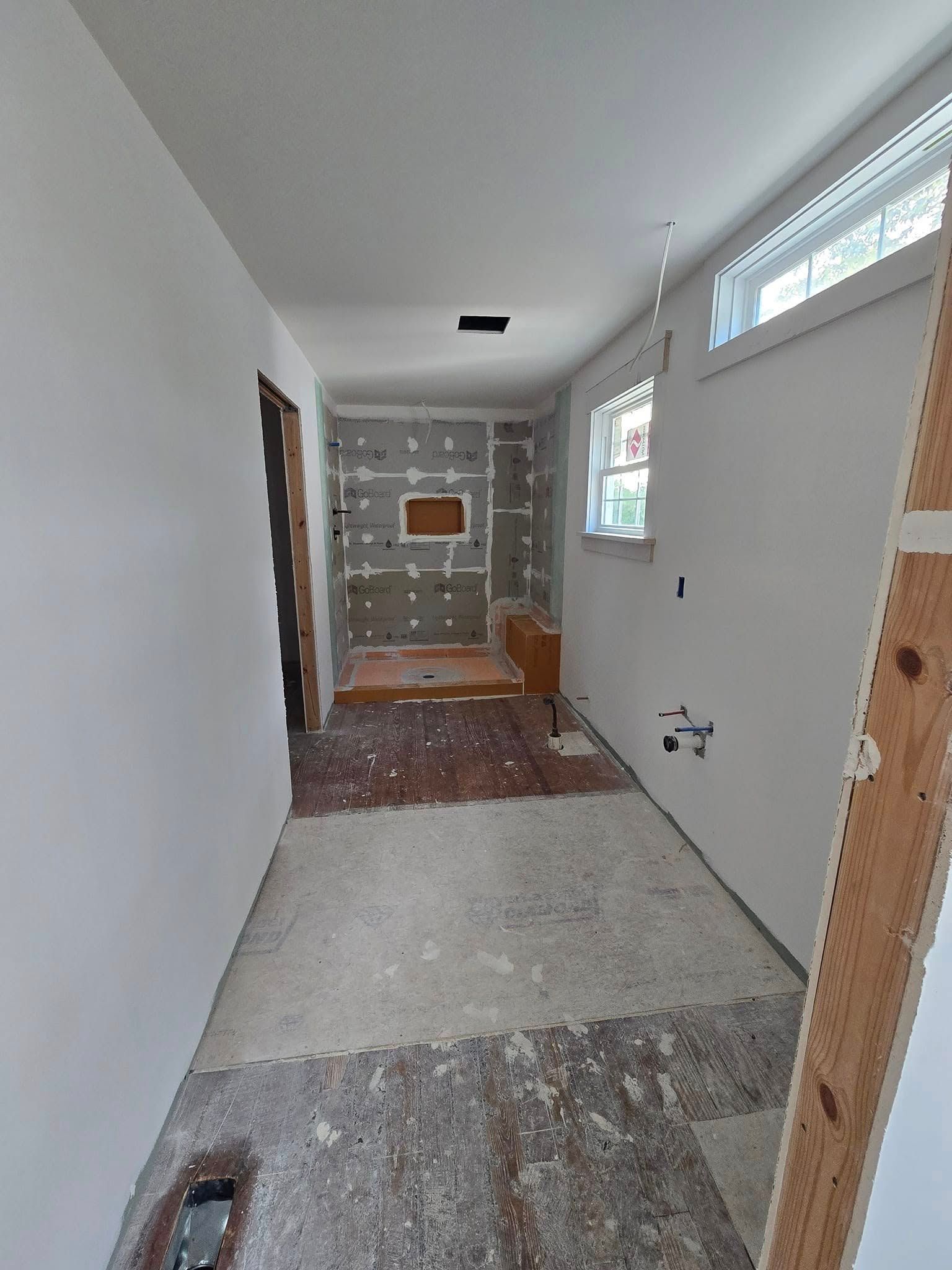 A long hallway with white walls and a window in a house under construction.